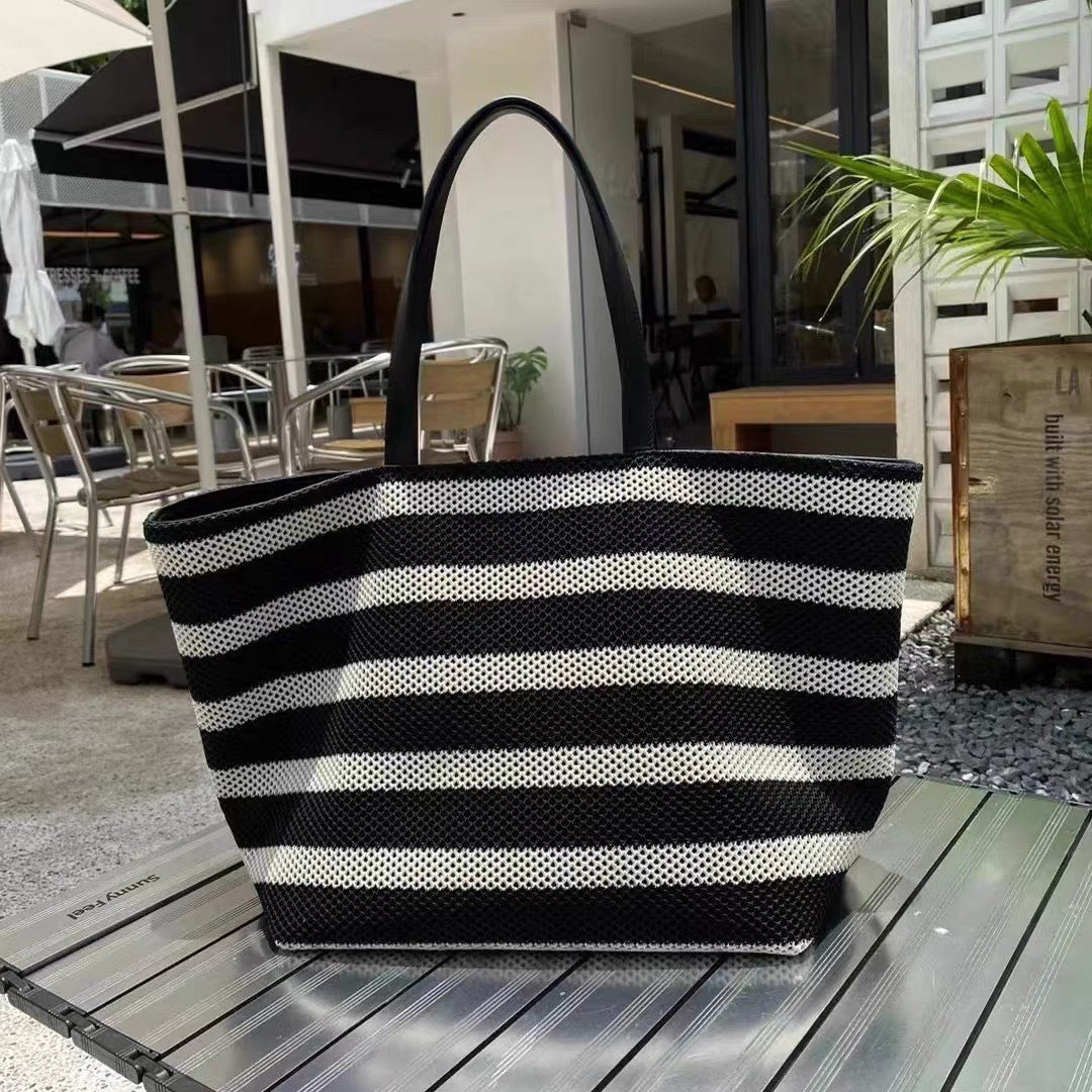 Black and white striped tote bag on a wooden surface with an outdoor setting in the background
