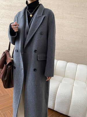 Person wearing an old money style wool coat holding a brown bag in an indoor setting.