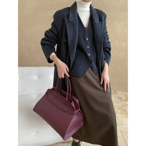 Person wearing a dark coat and holding a maroon handbag against a neutral background