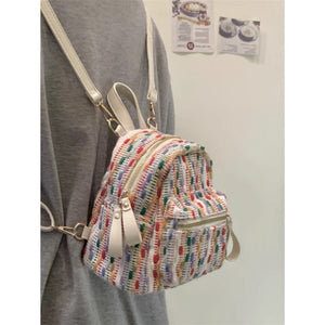 Multicolored striped backpack with gold accents worn over a gray shirt against a white wall.