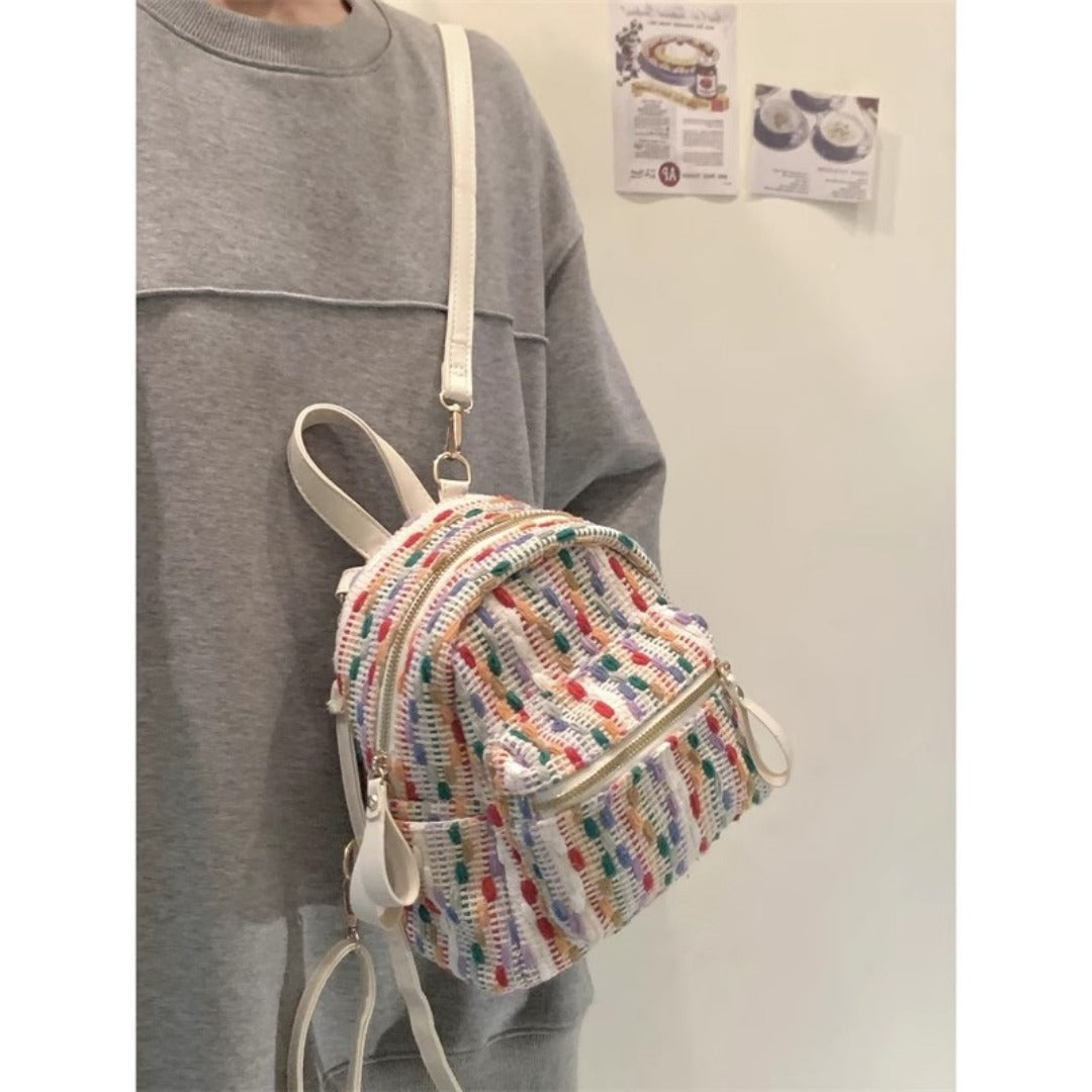 Person wearing a colorful mini backpack with a plain background