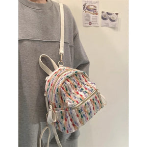 Person wearing a colorful mini backpack with a plain background