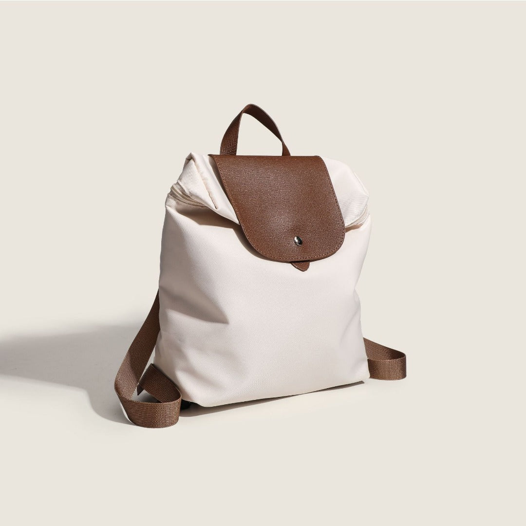 nylon commuter backpack purse with brown leather flap and strap on a light beige background