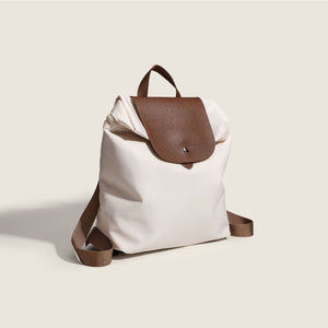 nylon commuter backpack purse with brown leather flap and strap on a light beige background
