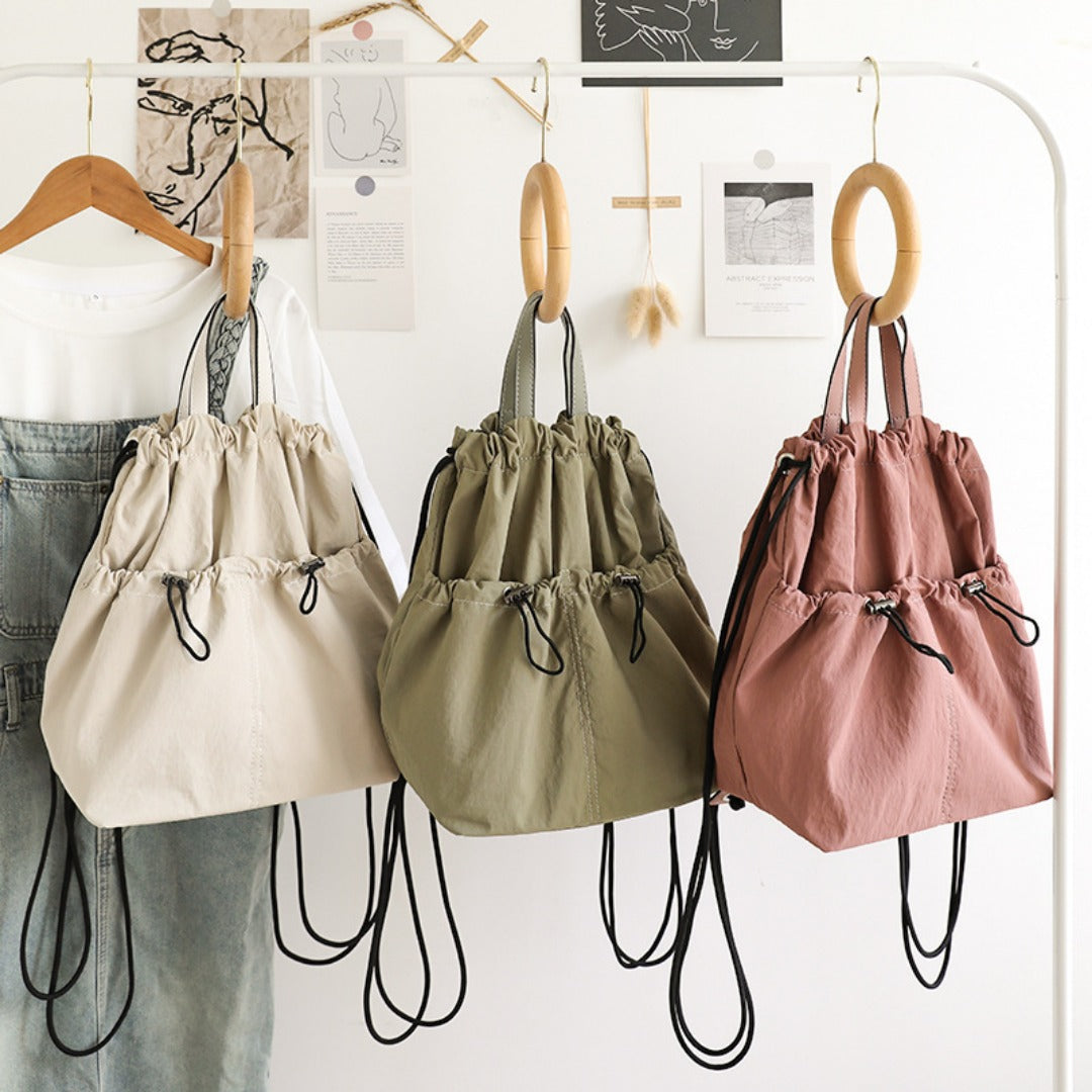 Three drawstring bags in beige, green, and pink hanging on a rack.