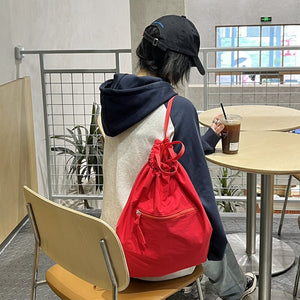 Person sitting at a table with a red backpack, drinking from a cup.