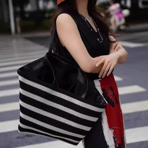 Person holding a black and white striped tote bag on a street.