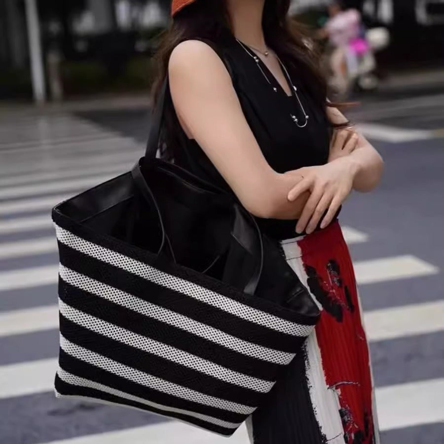 Person holding a black and white striped tote bag on a street.