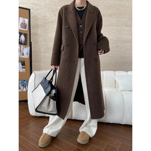 Person wearing an old money style wool coat in a room with a white couch and framed pictures on the wall.