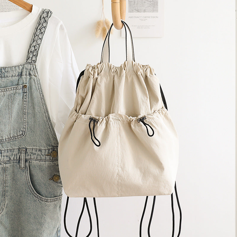 Beige drawstring bag hanging on a wooden hanger against a white background.