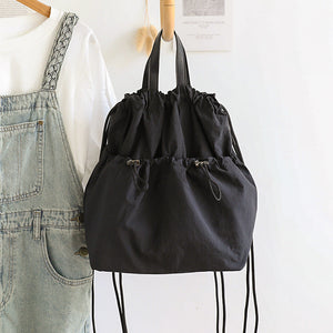 Black drawstring bag hanging on a wooden hanger with denim overalls and a white shirt in the background.