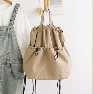 Beige drawstring bag hanging on a wooden hanger against a white background.