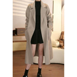Person wearing a long beige coat over a black dress in an indoor setting.