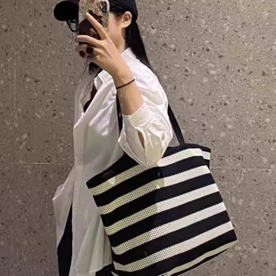 Person holding a black and white striped bag against a gray wall.