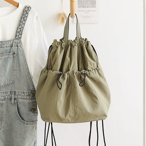 Khaki drawstring bag on a white background with denim overalls and a white shirt.