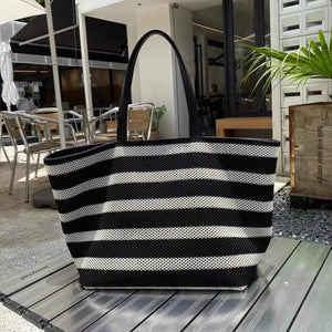 Black and white striped tote bag on a wooden surface with an outdoor setting in the background