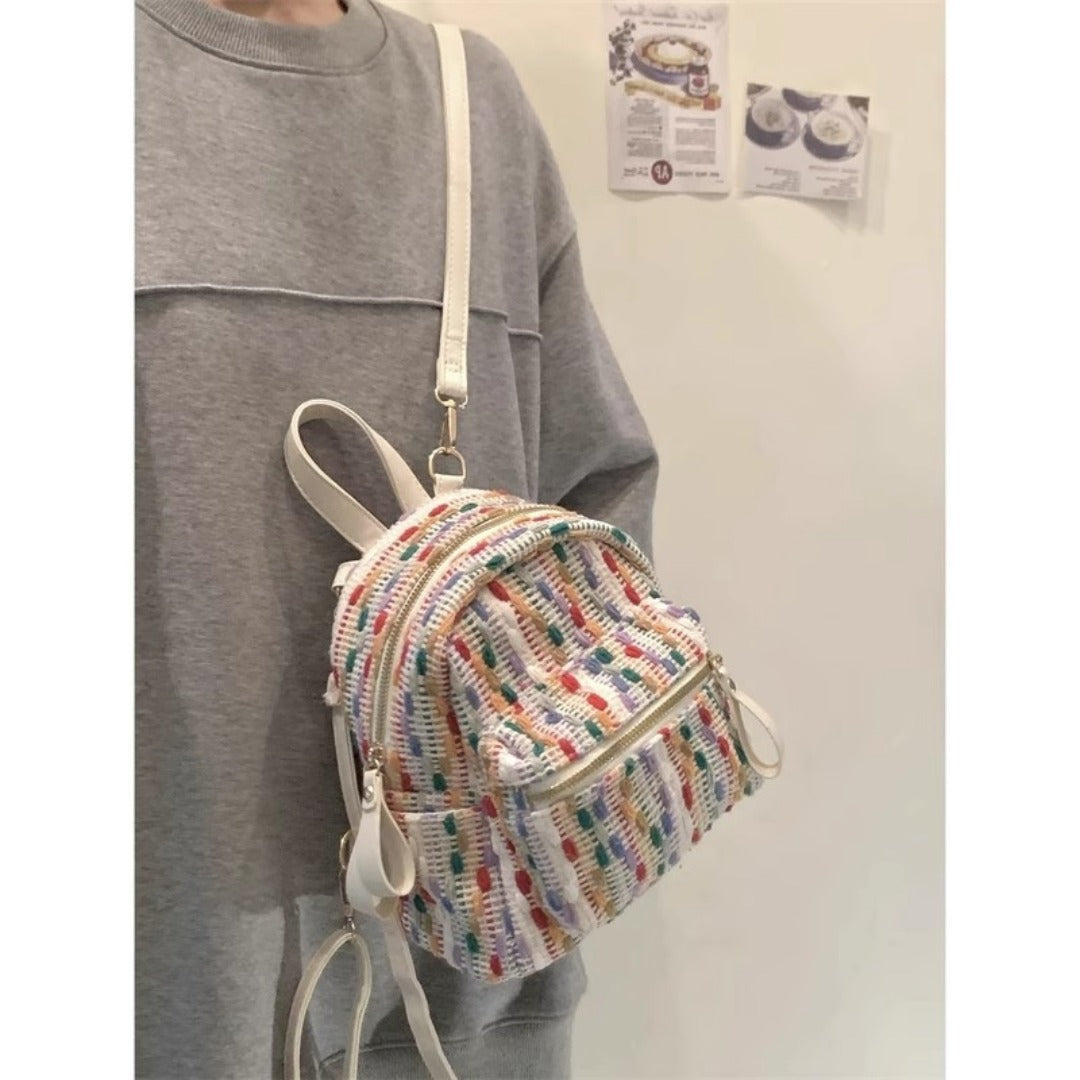 Person wearing a rainbow knit backpack with a plain background