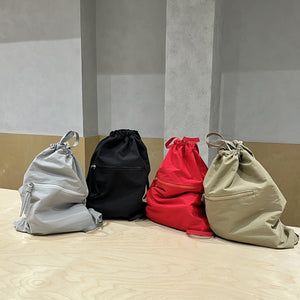Four lightweight nylon drawstring backpack purse in gray, black, red, and beige on a wooden surface with a neutral background.