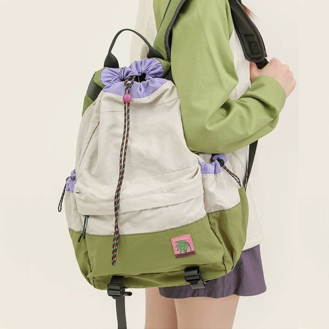 Person wearing a green and beige backpack with a purple drawstring on a plain background
