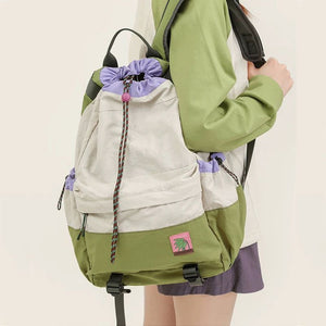 Person wearing a green and beige backpack with a purple drawstring on a plain background