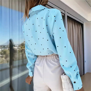 Person wearing a light blue shirt with black polka dots and white pants, standing indoors.